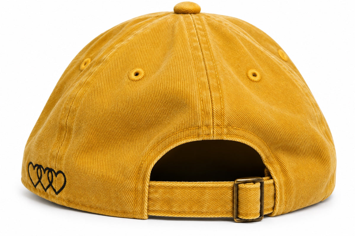 Washed mustard dad hat showing adjustable buckle strap and black signature hearts