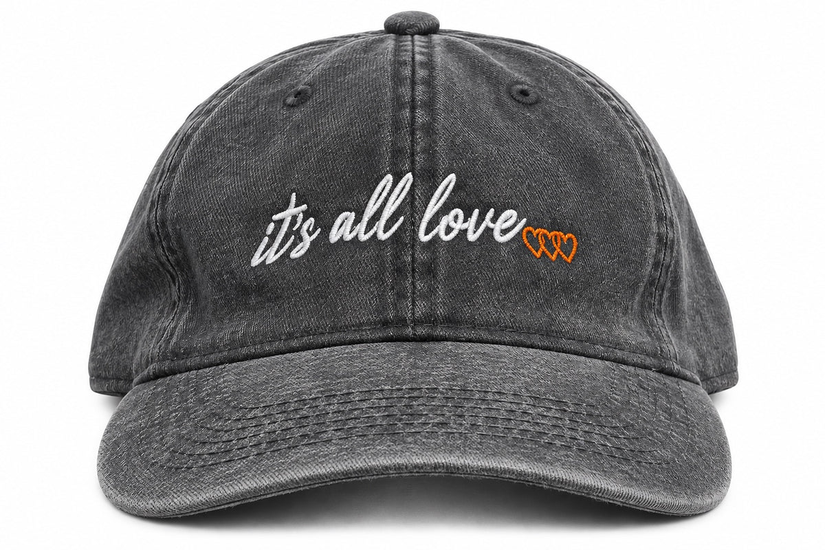 Washed grey dad hat with white it’s all love script and three orange signature hearts embroidered on front